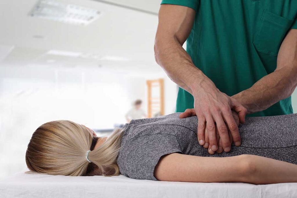 Athlete receiving a careful back adjustment while a clinician observes movement in a bright treatment room.