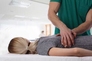 Athlete receiving a careful back adjustment while a clinician observes movement in a bright treatment room.