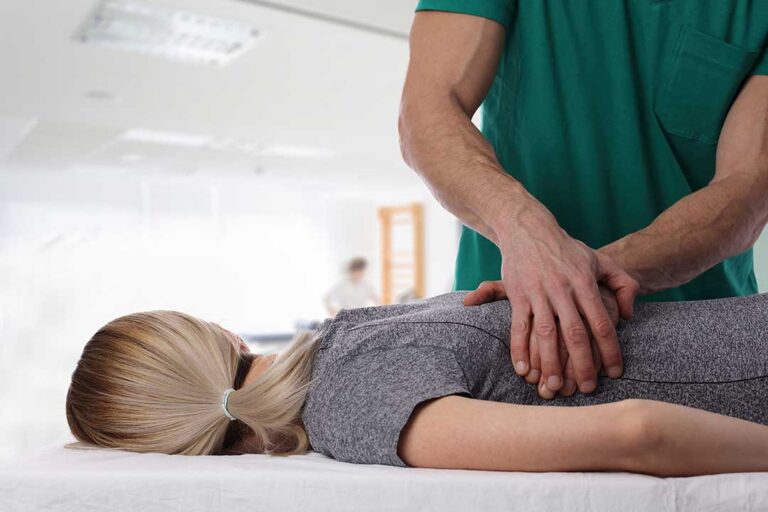 Athlete receiving a careful back adjustment while a clinician observes movement in a bright treatment room.