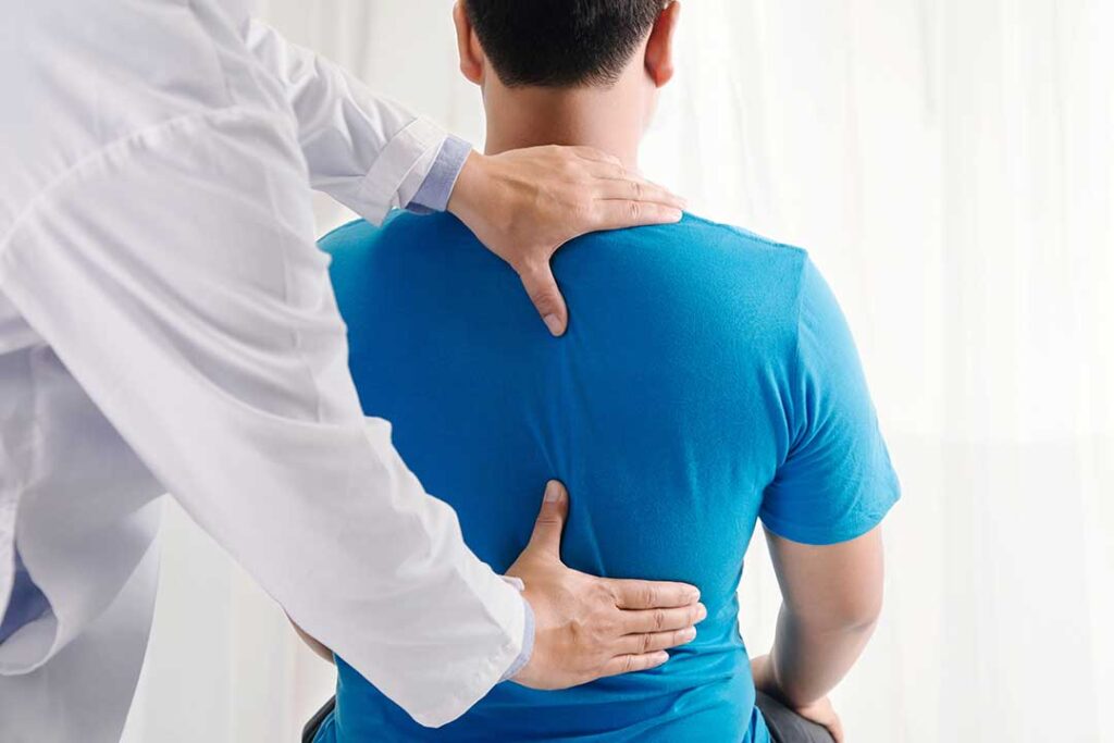 Patient discusses back pain with a chiropractor during an examination in a bright clinical room.